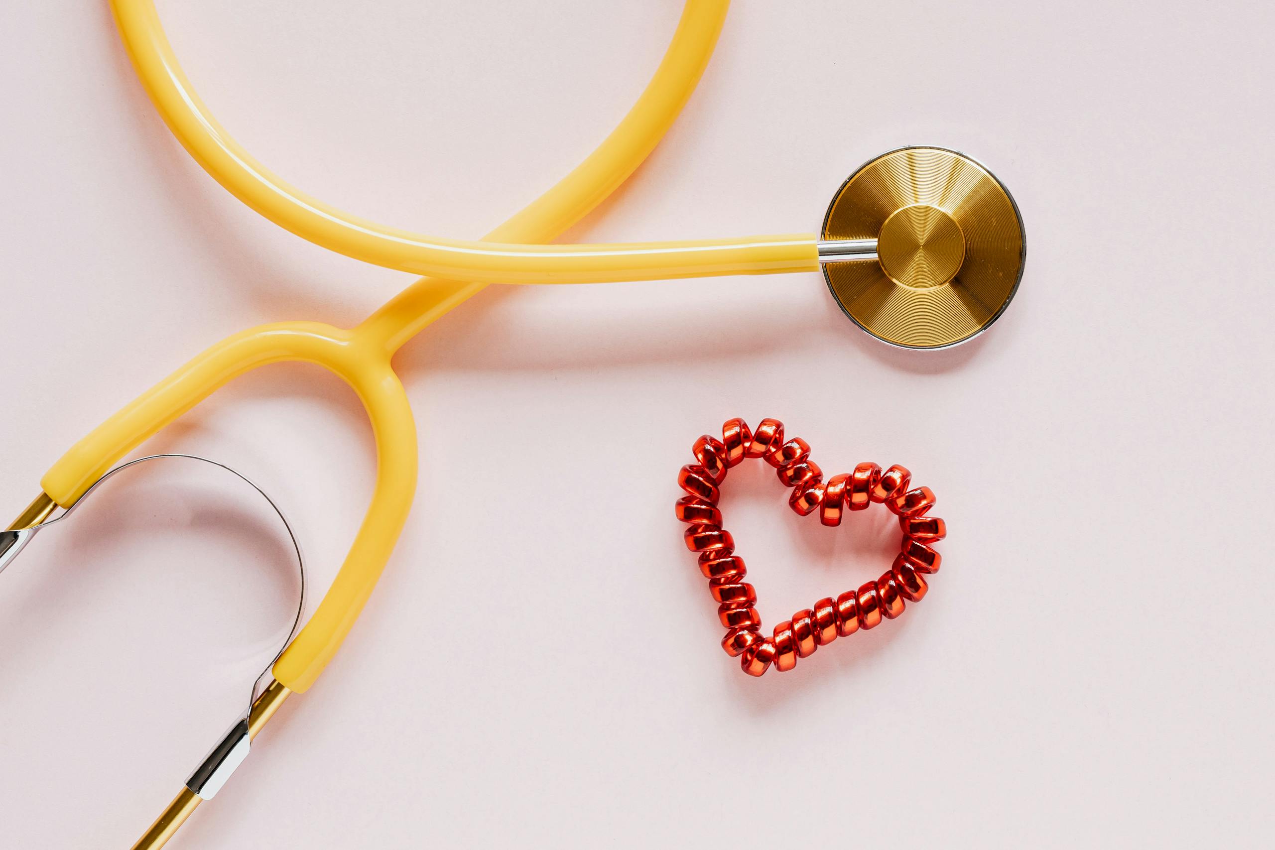 A yellow stethoscope and red heart decoration symbolize love and healthcare on soft pink.